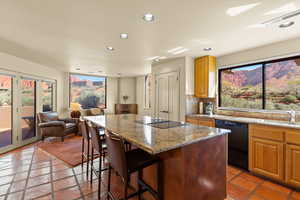 Kitchen featuring light stone countertops, black appliances, a kitchen bar, a center island, and tasteful backsplash