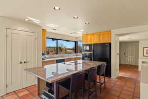Kitchen with dark stone counters, black appliances, recessed lighting, a center island, and a breakfast bar