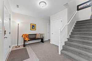 Foyer with stairs and light colored carpet