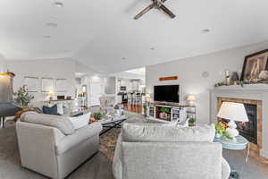 Living room featuring a ceiling fan, a tiled fireplace, carpet floors, and vaulted ceiling