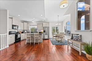 Kitchen featuring a breakfast bar, black appliances, dark wood-style flooring, a kitchen island, and hanging lights