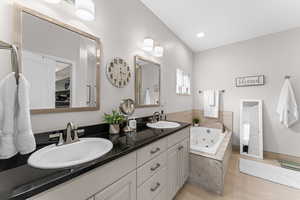 Full bathroom with double vanity, a jetted tub, and light wood-type flooring