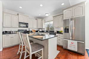 Kitchen featuring black appliances, a kitchen breakfast bar, dark wood-style flooring, a kitchen island, and recessed lighting