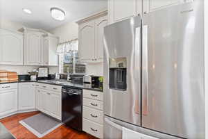Kitchen with stainless steel fridge, dishwasher, dark countertops, and dark wood finished floors