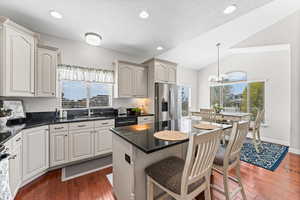 Kitchen with dark stone countertops, a kitchen island, a kitchen breakfast bar, dark wood-style flooring, and vaulted ceiling