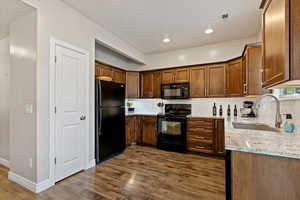 Kitchen with black appliances, light stone countertops, decorative backsplash, dark wood-style flooring, and recessed lighting