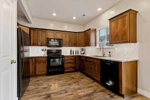 Kitchen with black appliances, dark wood finished floors, light stone countertops, recessed lighting, and backsplash