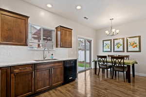 Kitchen featuring backsplash, light stone countertops, black dishwasher, a chandelier, and dark wood finished floors