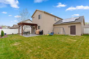 Back of house with solar panels, a fenced backyard, a patio, and a pergola