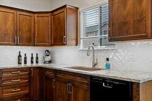 Kitchen with light stone counters, backsplash, and black dishwasher
