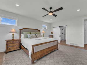 Bedroom with a barn door, wood finished floors, a ceiling fan, recessed lighting, and ensuite bath