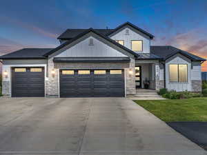 View of front of house with board and batten siding, stone siding, a standing seam roof, an attached garage, and concrete driveway