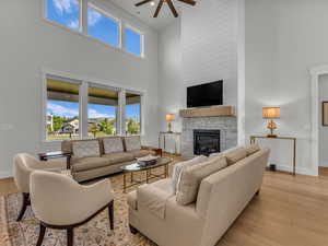 Living room featuring light wood-style floors, ceiling fan, a high ceiling, and a stone fireplace