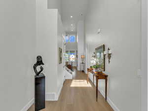 Hallway featuring a high ceiling, light wood-style flooring, and recessed lighting