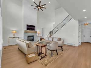 Living area with a high ceiling, light wood-style flooring, a stone fireplace, a ceiling fan, and recessed lighting