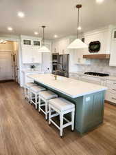 Two tone kitchen with glass insert cabinets, dual tone cabinetry, a center island with sink, pendant lighting, and a breakfast bar