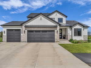 Modern farmhouse with an attached garage, board and batten siding, stone siding, a standing seam roof, and driveway