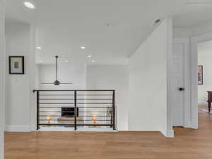 Hallway featuring light wood-style flooring, recessed lighting, and an upstairs landing