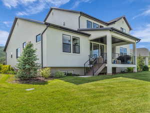 Back of house with a lawn, stucco siding, and covered porch