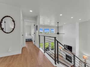 Corridor with an upstairs landing, light wood-style flooring, and recessed lighting