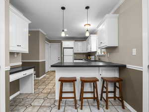Kitchen featuring a breakfast bar, ornamental molding, dark countertops, white cabinets, and freestanding refrigerator