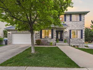 View of front of house with driveway, a yard, a garage, and brick siding