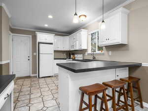 Kitchen featuring a breakfast bar area, dark countertops, white cabinets, white appliances, and crown molding