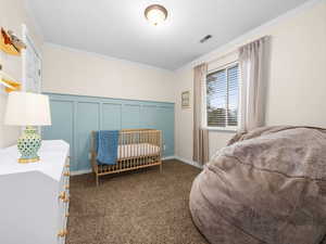 Bedroom featuring ornamental molding, a decorative wall, a nursery area, and dark carpet