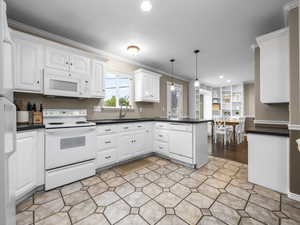 Kitchen with a peninsula, white appliances, ornamental molding, dark countertops, and pendant lighting