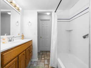 Full bathroom featuring light stone finish floors, vanity, shower / bath combination with curtain, and a textured ceiling