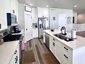 Kitchen with stainless steel appliances, dark wood-style floors, a kitchen island with sink, white cabinets, and a textured ceiling