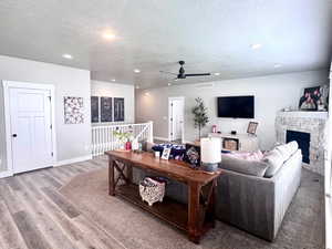 Living room with a fireplace, wood finished floors, a textured ceiling, ceiling fan, and recessed lighting