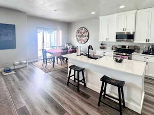 Kitchen with stainless steel appliances, a kitchen bar, white cabinetry, an island with sink, and a textured ceiling