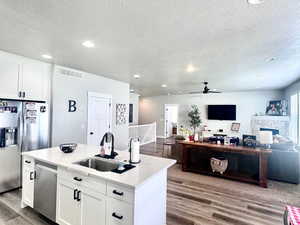 Kitchen featuring a kitchen island with sink, open floor plan, light wood finished floors, white cabinetry, and stainless steel appliances