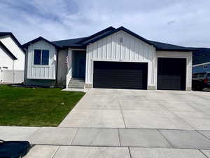 View of front of home with board and batten siding, an attached garage, a front yard, and driveway