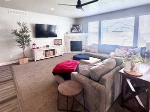 Living room featuring a textured ceiling, ceiling fan, a stone fireplace, and wood finished floors