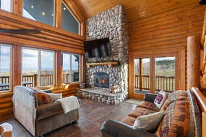 Living area with rustic walls, a vaulted wooden ceiling, a stone fireplace, and french doors
