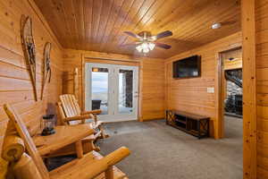 Living area with wooden walls, ceiling fan, light colored carpet, and wood ceiling