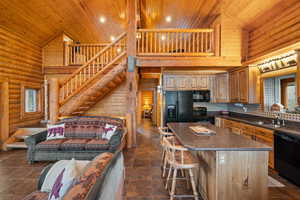 Kitchen with rustic walls, a kitchen bar, black appliances, a vaulted wood ceiling, and a center island