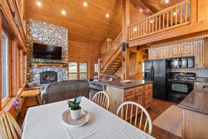 Dining space featuring rustic walls, a vaulted wooden ceiling, a stone fireplace, and recessed lighting