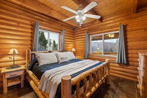 Bedroom featuring log walls, ceiling fan, and a wooden ceiling with exposed beams