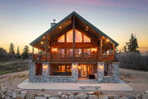 Back of house at dusk with stone siding, a patio area, and a chimney