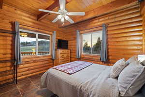 Bedroom with a wood ceiling with exposed beams, ceiling fan, log walls, and dark tile patterned flooring