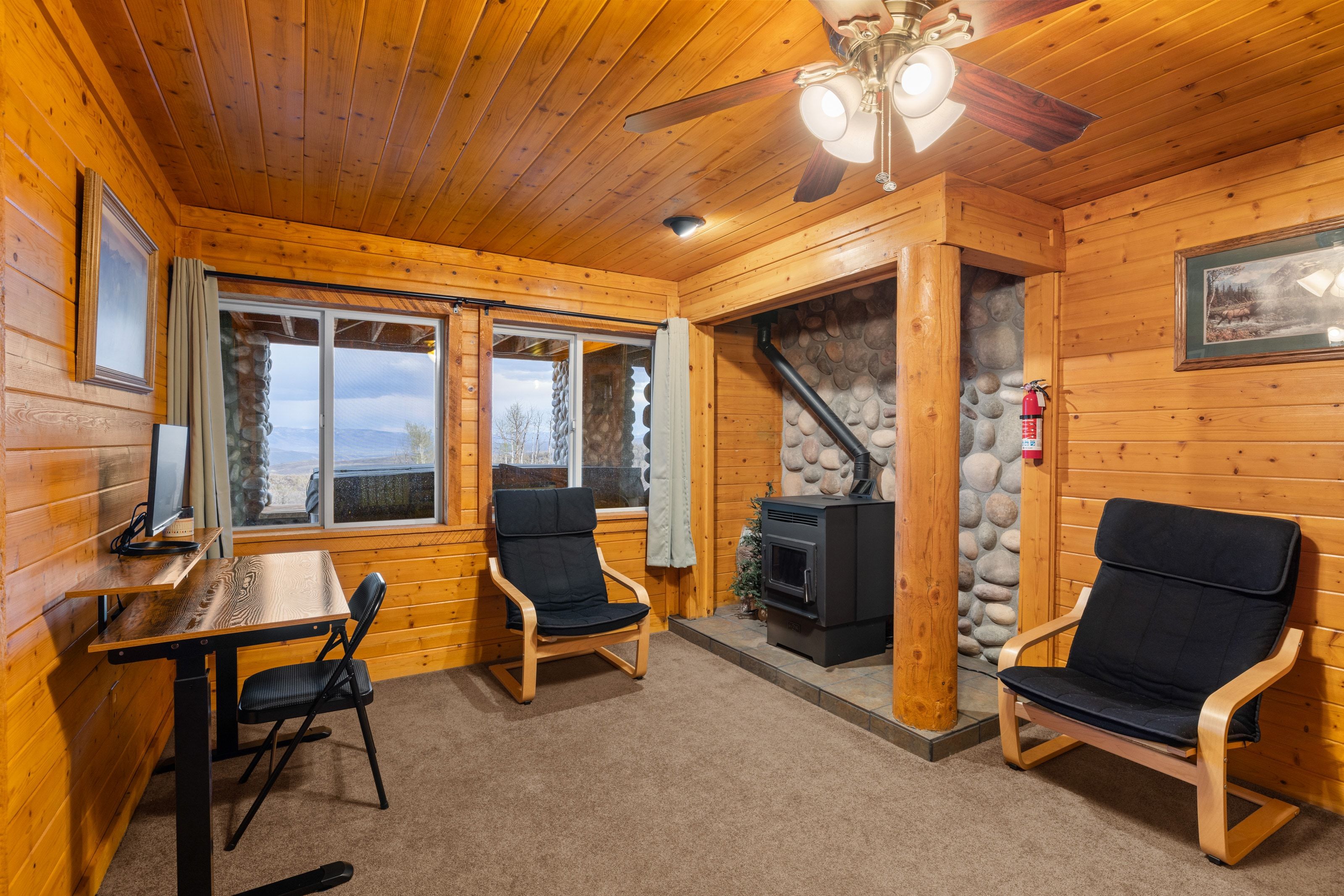 Office space with wooden walls, light colored carpet, a wood stove, a ceiling fan, and wood ceiling