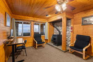 Office space with wooden walls, light colored carpet, a wood stove, a ceiling fan, and wood ceiling