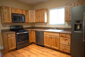 Kitchen featuring stainless steel appliances, light wood-type flooring, dark countertops, and light wood finish cabinetry