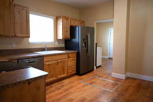 Kitchen with dark countertops, black dishwasher, stainless steel fridge with ice dispenser, and light wood-style floors