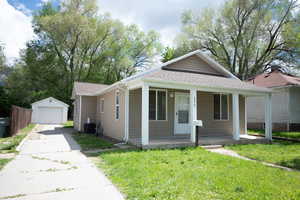 Bungalow with a porch, a detached garage, a shingled roof, an outdoor structure, and a front lawn