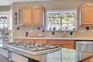 Kitchen featuring stainless steel gas cooktop, dark stone countertops, healthy amount of natural light, and tasteful backsplash