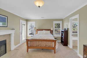Bedroom featuring a fireplace, light colored carpet, multiple windows, ornamental molding, and access to exterior